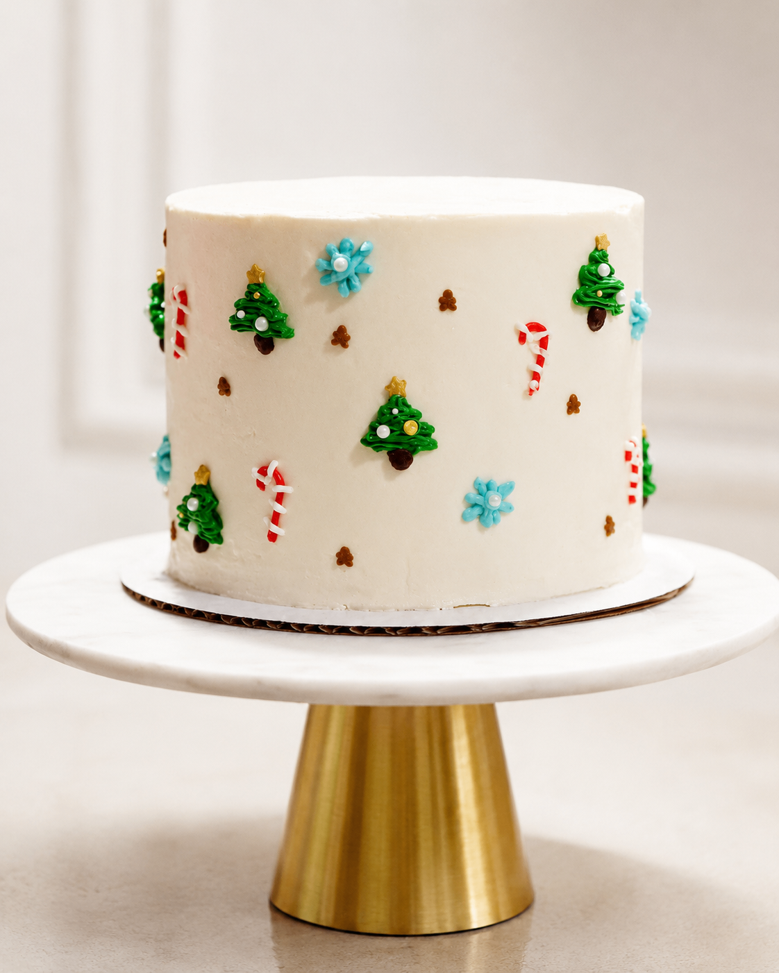 Mini white buttercream cake with piped holiday details displayed on a gold pedestal stand