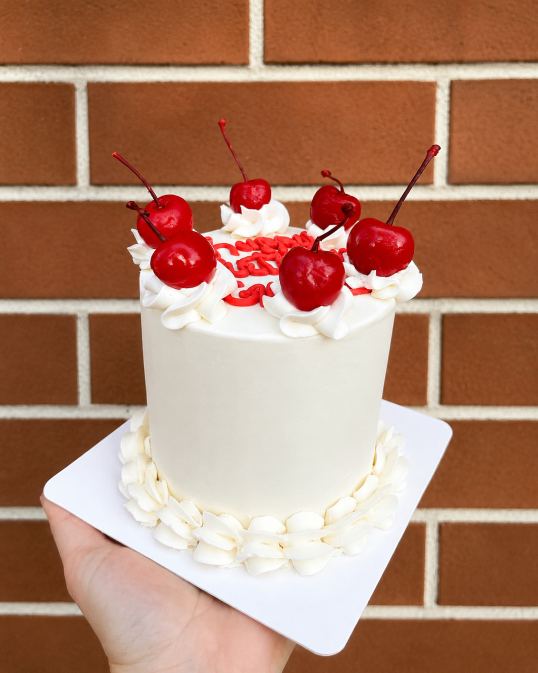 White buttercream mini cake topped with cherries against a Charleston brick backdrop