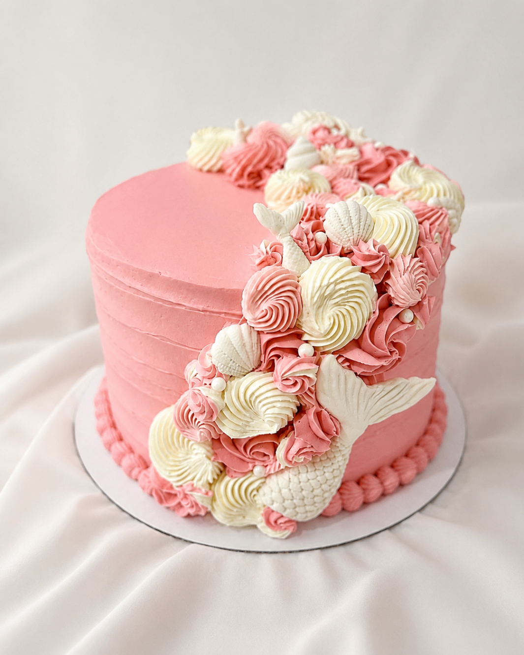 Blush buttercream celebration cake with seashell-inspired piping and sculpted mermaid tail details