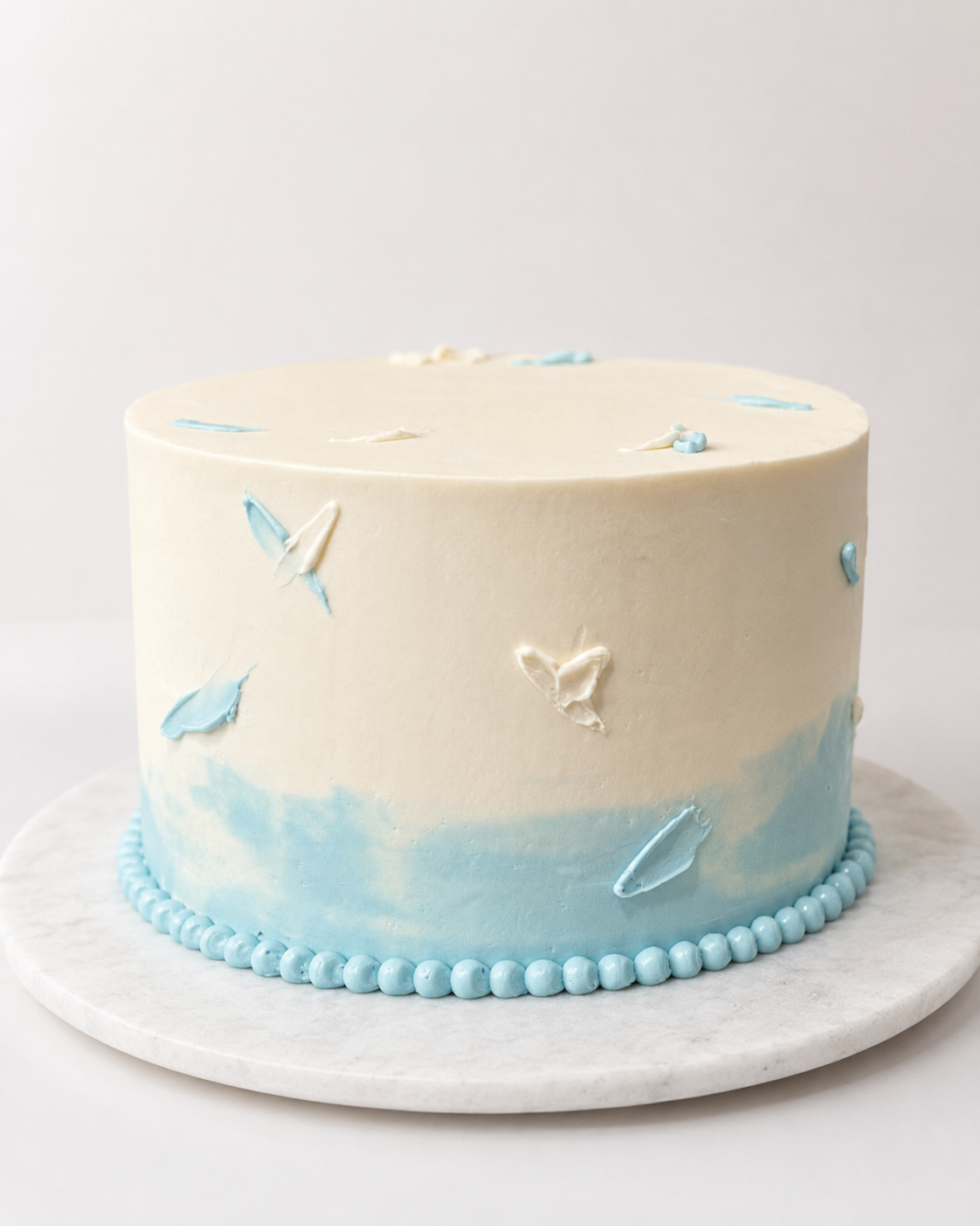 White buttercream cake with soft blue butterfly details on a marble stand