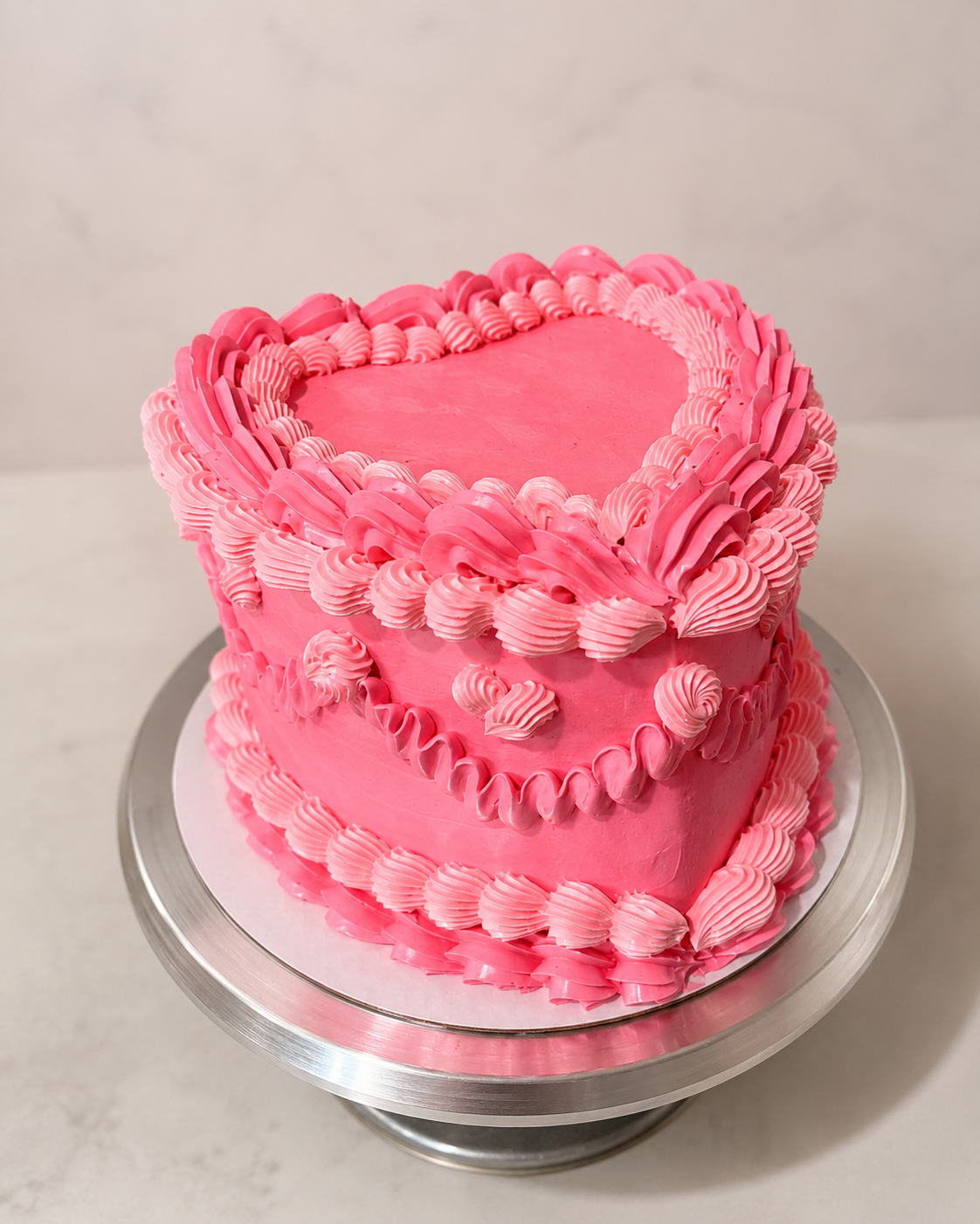 Pink heart-shaped cake with vintage shell piping on a silver cake stand